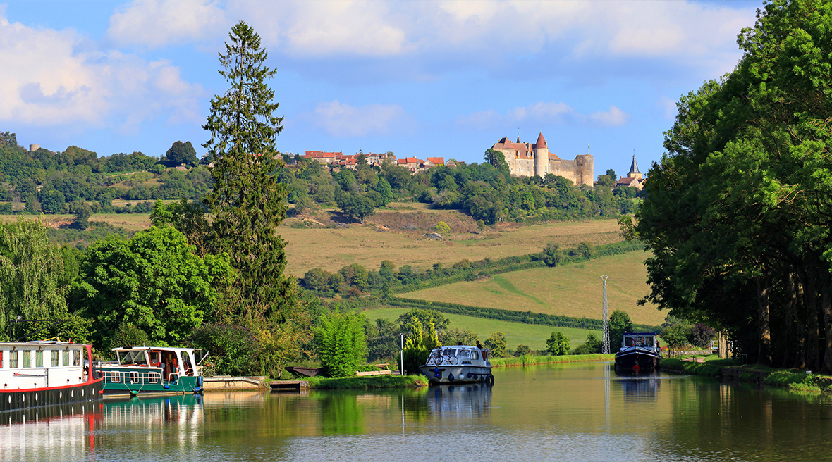 boats on a canal with trees on the waterside and a chateau in the distance